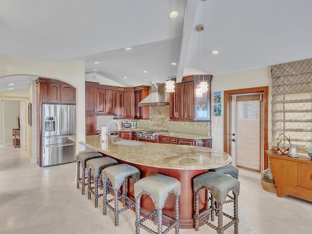 kitchen with pendant lighting, an island with sink, wall chimney exhaust hood, stainless steel appliances, and vaulted ceiling