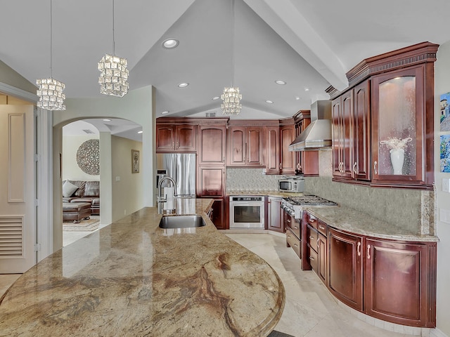 kitchen with wall chimney range hood, pendant lighting, tasteful backsplash, sink, and appliances with stainless steel finishes