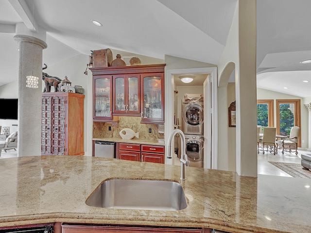 kitchen with ornate columns, stacked washer and clothes dryer, vaulted ceiling, sink, and backsplash