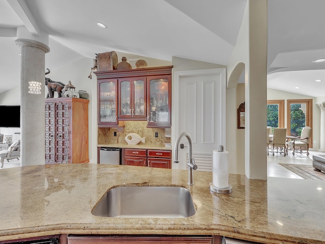 kitchen featuring lofted ceiling, sink, backsplash, dishwasher, and decorative columns