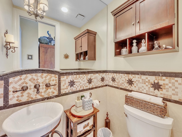 bathroom featuring a notable chandelier, tile walls, toilet, and sink