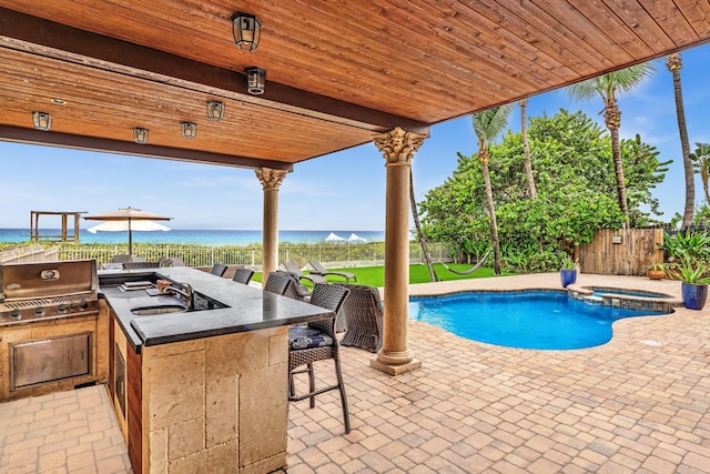 view of pool with a water view, grilling area, an outdoor kitchen, a patio, and an in ground hot tub