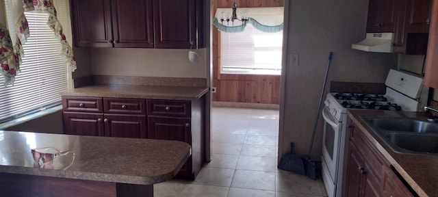 kitchen featuring white gas stove, kitchen peninsula, an inviting chandelier, exhaust hood, and light tile patterned floors