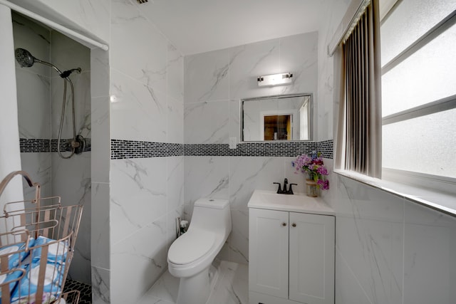 bathroom with a tile shower, tile walls, vanity, and toilet