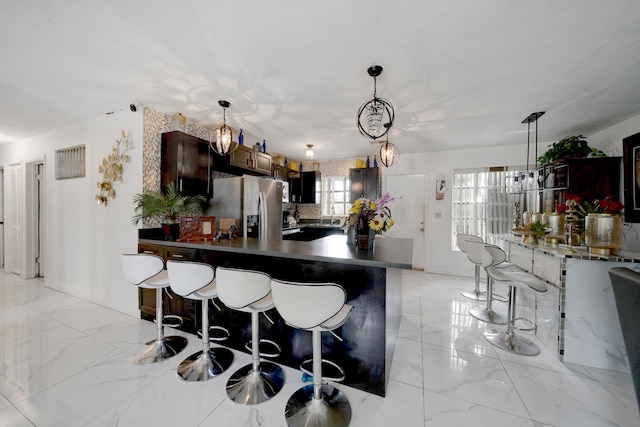 kitchen with a kitchen breakfast bar, stainless steel refrigerator with ice dispenser, hanging light fixtures, and dark brown cabinetry