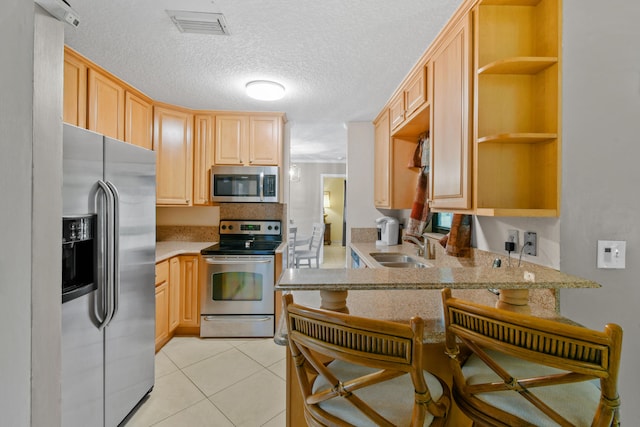 kitchen with kitchen peninsula, a kitchen breakfast bar, stainless steel appliances, light brown cabinets, and light tile patterned flooring