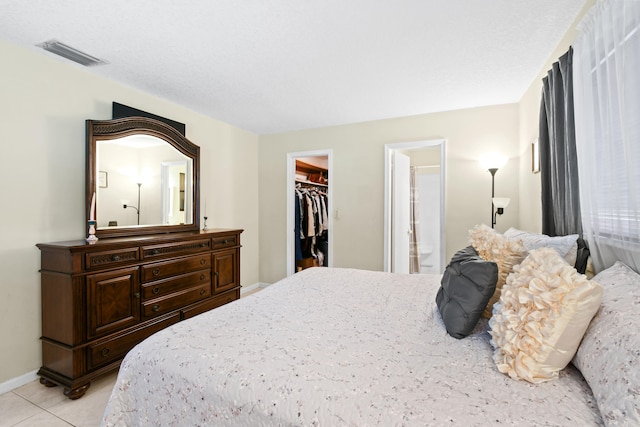 bedroom with connected bathroom, a walk in closet, a closet, and light tile patterned flooring