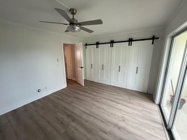 unfurnished bedroom with ceiling fan, a closet, light wood-type flooring, and a barn door