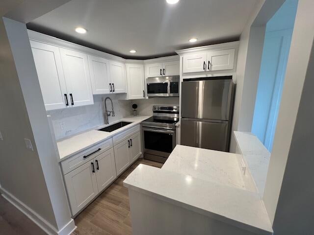 kitchen with appliances with stainless steel finishes, white cabinetry, sink, and light hardwood / wood-style flooring