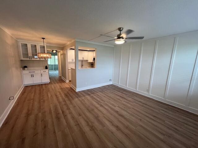 unfurnished living room with ceiling fan with notable chandelier, dark wood-type flooring, and crown molding