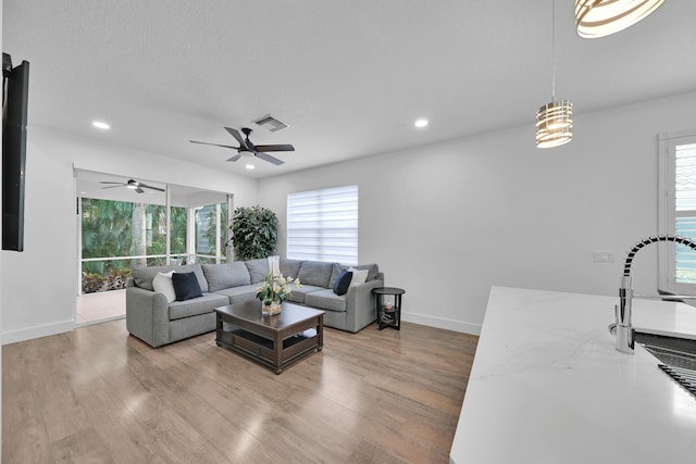 living room featuring ceiling fan, light hardwood / wood-style floors, and a textured ceiling