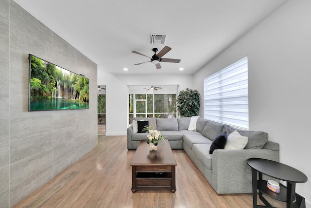 living room with a textured ceiling, ceiling fan, light hardwood / wood-style floors, and tile walls