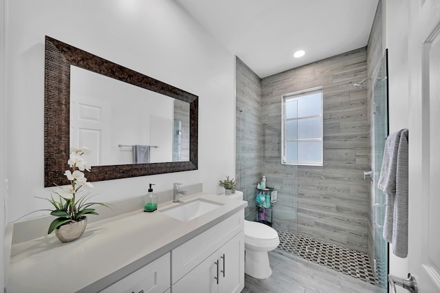 bathroom featuring a tile shower, vanity, hardwood / wood-style flooring, and toilet