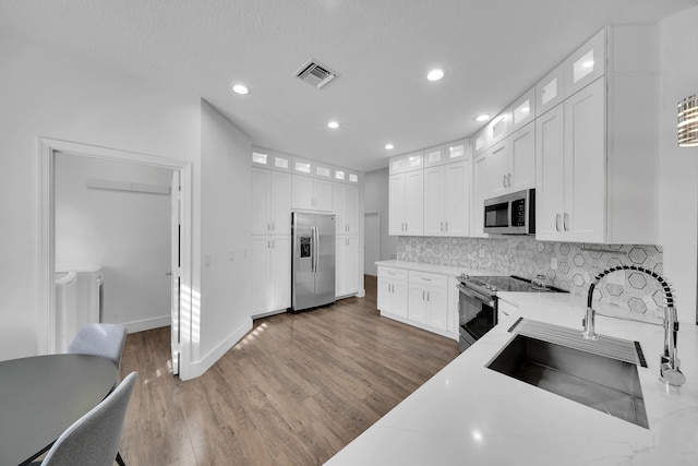 kitchen featuring white cabinets, appliances with stainless steel finishes, tasteful backsplash, and hardwood / wood-style floors