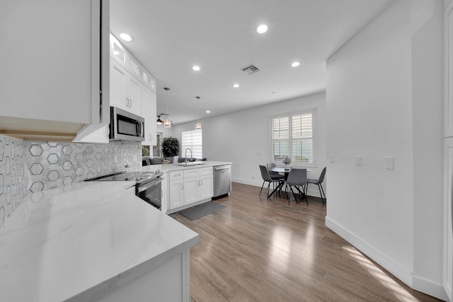 kitchen with kitchen peninsula, appliances with stainless steel finishes, wood-type flooring, decorative light fixtures, and white cabinets