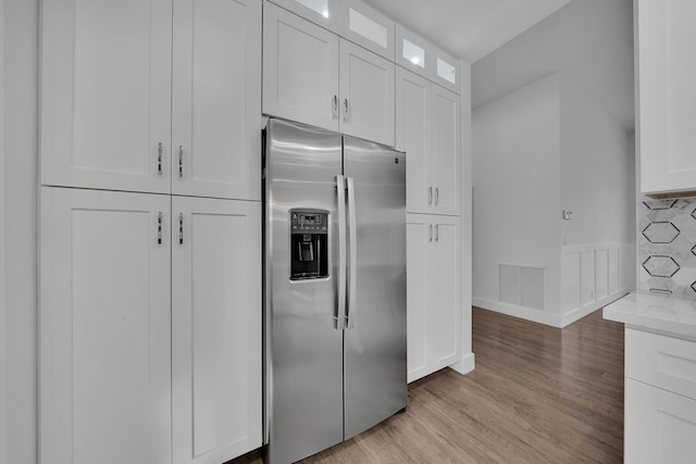 kitchen with light stone countertops, white cabinetry, light wood-type flooring, and stainless steel fridge with ice dispenser