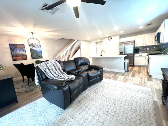 living room with light hardwood / wood-style floors, sink, and ceiling fan with notable chandelier