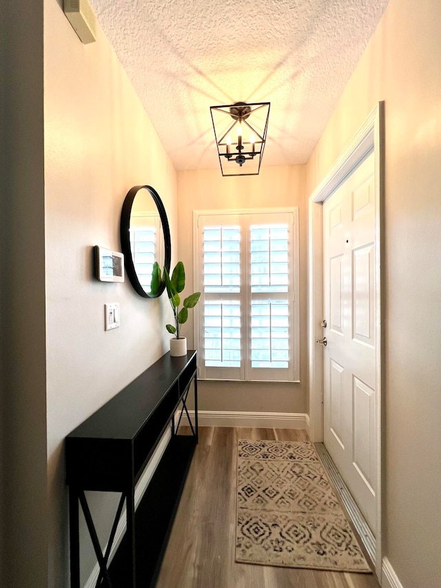 doorway to outside featuring an inviting chandelier, a textured ceiling, and wood-type flooring