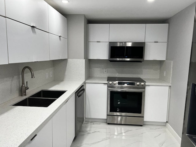 kitchen with stainless steel appliances, white cabinetry, light stone counters, and sink