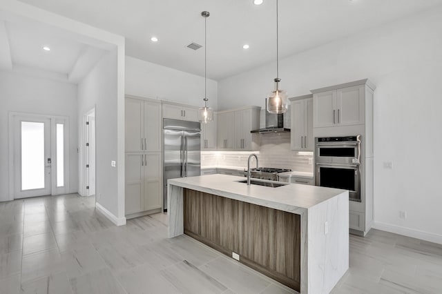 10125 Driftwood Way, Palm Beach Gardens, FL 33412 - kitchen with stainless steel appliances, decorative backsplash, wall chimney exhaust hood, light countertops, and a kitchen island with sink