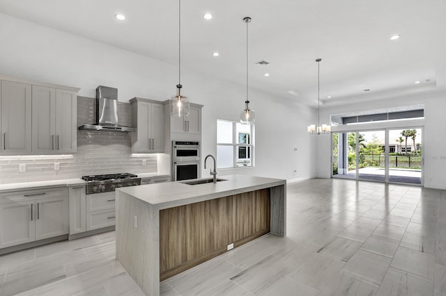 10125 Driftwood Way, Palm Beach Gardens, FL 33412 - kitchen featuring stainless steel appliances, wall chimney exhaust hood, backsplash, an island with sink, and light countertops