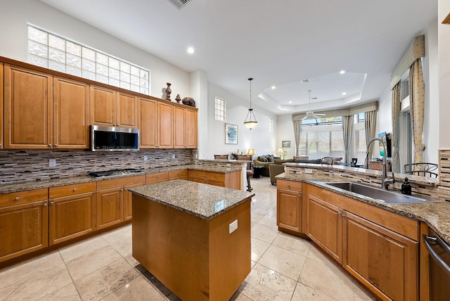 kitchen with a raised ceiling, sink, backsplash, stainless steel appliances, and a center island