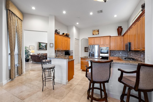 kitchen with a kitchen breakfast bar, kitchen peninsula, appliances with stainless steel finishes, and stone counters