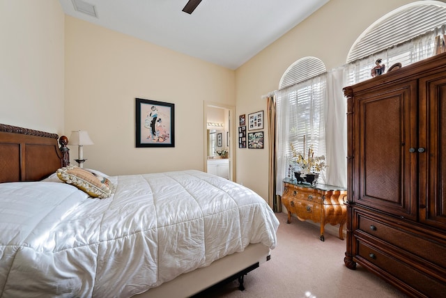 bedroom featuring ceiling fan, vaulted ceiling, light carpet, and ensuite bathroom