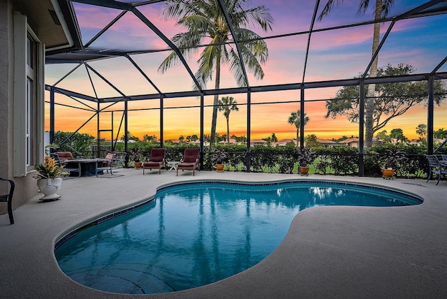 pool at dusk featuring glass enclosure and a patio