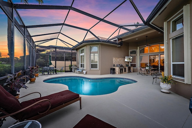 pool at dusk with a patio, glass enclosure, and an outdoor kitchen