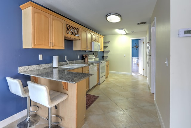 kitchen featuring a sink, visible vents, stone countertops, a kitchen bar, and white appliances