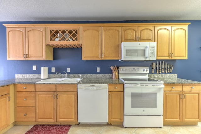 kitchen featuring stone countertops, light tile patterned floors, white appliances, and a sink