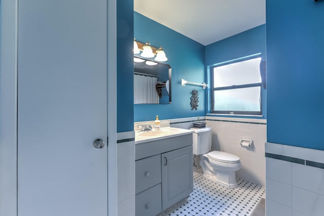bathroom with tile walls, vanity, tile patterned floors, toilet, and a wainscoted wall