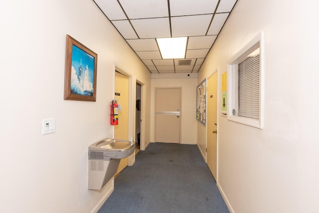 corridor with baseboards, carpet flooring, and a drop ceiling