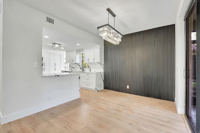 interior space featuring white cabinetry, light wood-type flooring, pendant lighting, sink, and kitchen peninsula