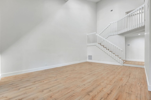 unfurnished living room featuring a towering ceiling and light wood-type flooring