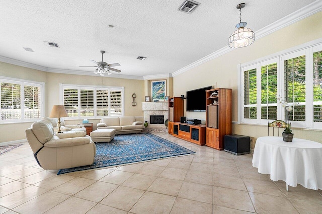 living room with a textured ceiling, light tile patterned flooring, a fireplace, ornamental molding, and ceiling fan