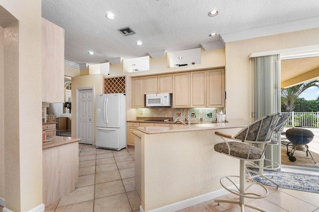 kitchen with a kitchen breakfast bar, white appliances, kitchen peninsula, crown molding, and light brown cabinetry