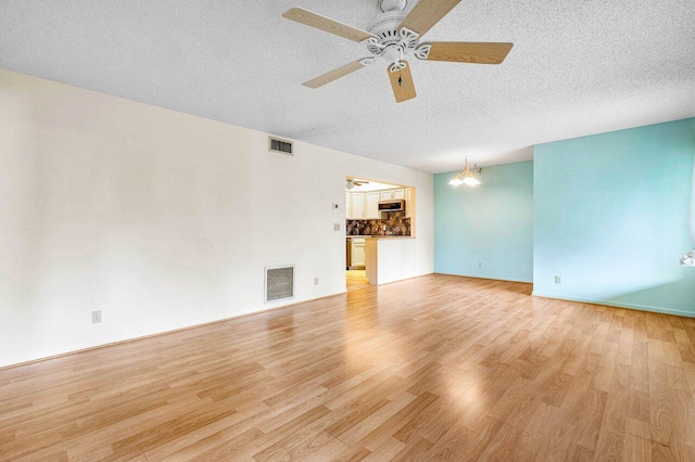 spare room featuring a textured ceiling, ceiling fan with notable chandelier, and light hardwood / wood-style floors