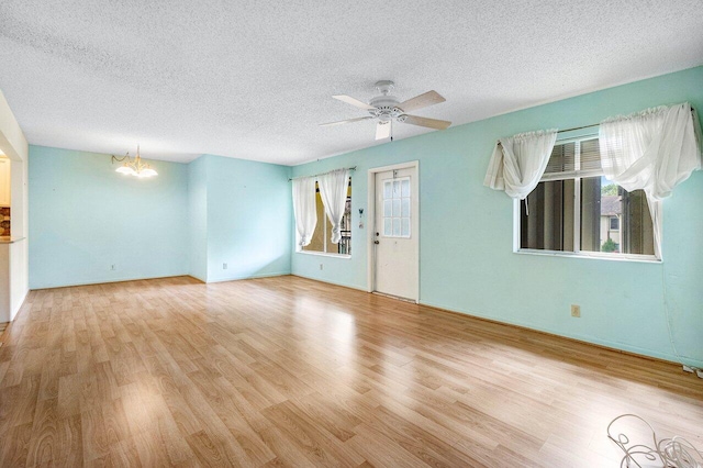 empty room with ceiling fan with notable chandelier, light wood-type flooring, and a textured ceiling