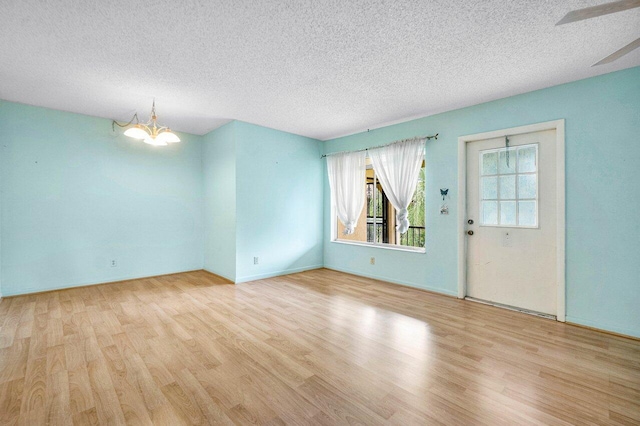 spare room with ceiling fan with notable chandelier, light hardwood / wood-style floors, and a textured ceiling