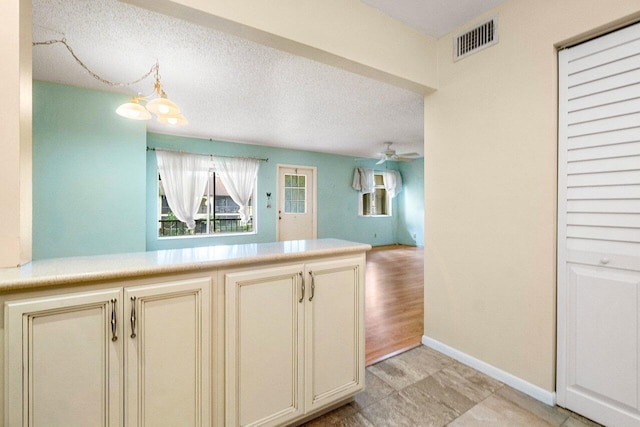 kitchen featuring a textured ceiling, ceiling fan with notable chandelier, cream cabinetry, and light hardwood / wood-style flooring