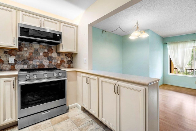 kitchen with kitchen peninsula, tasteful backsplash, cream cabinetry, appliances with stainless steel finishes, and a notable chandelier