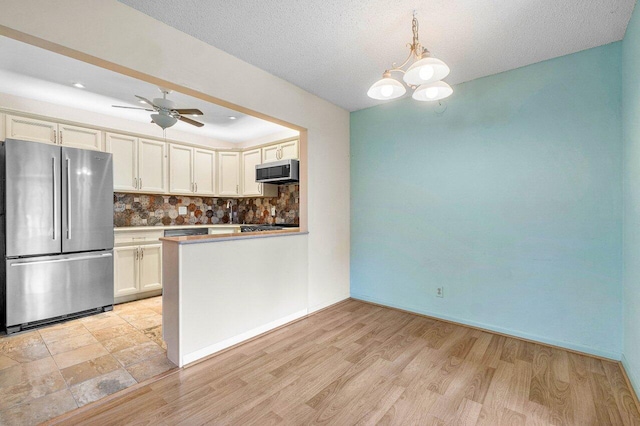 kitchen with ceiling fan with notable chandelier, appliances with stainless steel finishes, pendant lighting, and light hardwood / wood-style floors