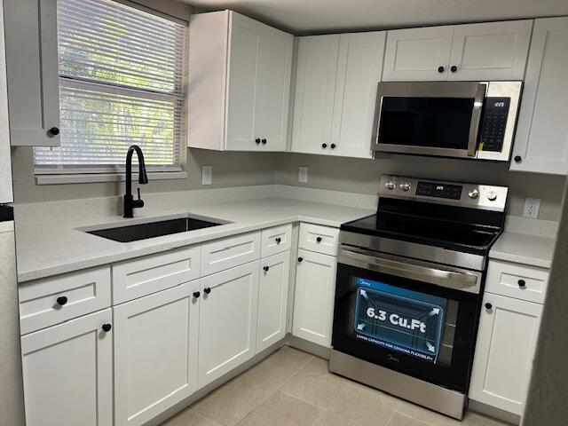 kitchen with sink, light tile patterned floors, white cabinets, and appliances with stainless steel finishes