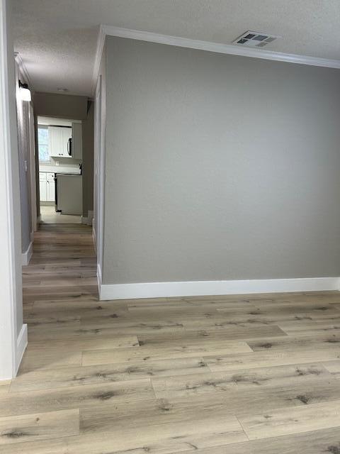 empty room featuring ornamental molding, a textured ceiling, and light wood-type flooring