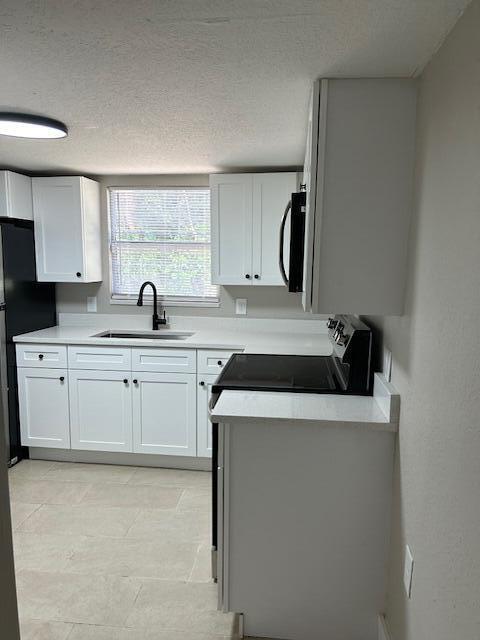 kitchen with stainless steel appliances, white cabinetry, light tile patterned flooring, and a textured ceiling