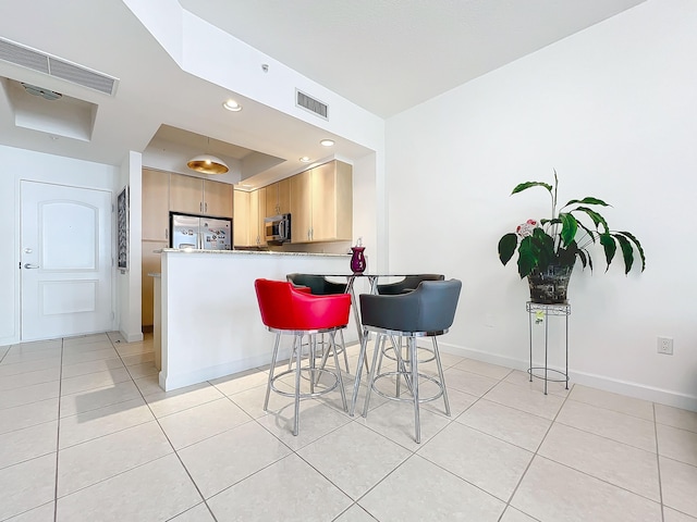 kitchen with light tile patterned flooring, appliances with stainless steel finishes, a breakfast bar area, and kitchen peninsula