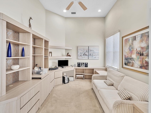 carpeted office featuring ceiling fan, a textured ceiling, built in desk, and a towering ceiling