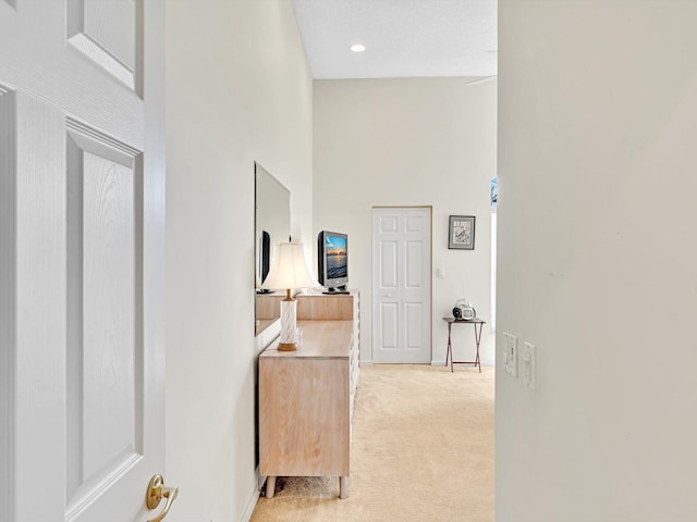 corridor featuring a towering ceiling, a textured ceiling, and light colored carpet